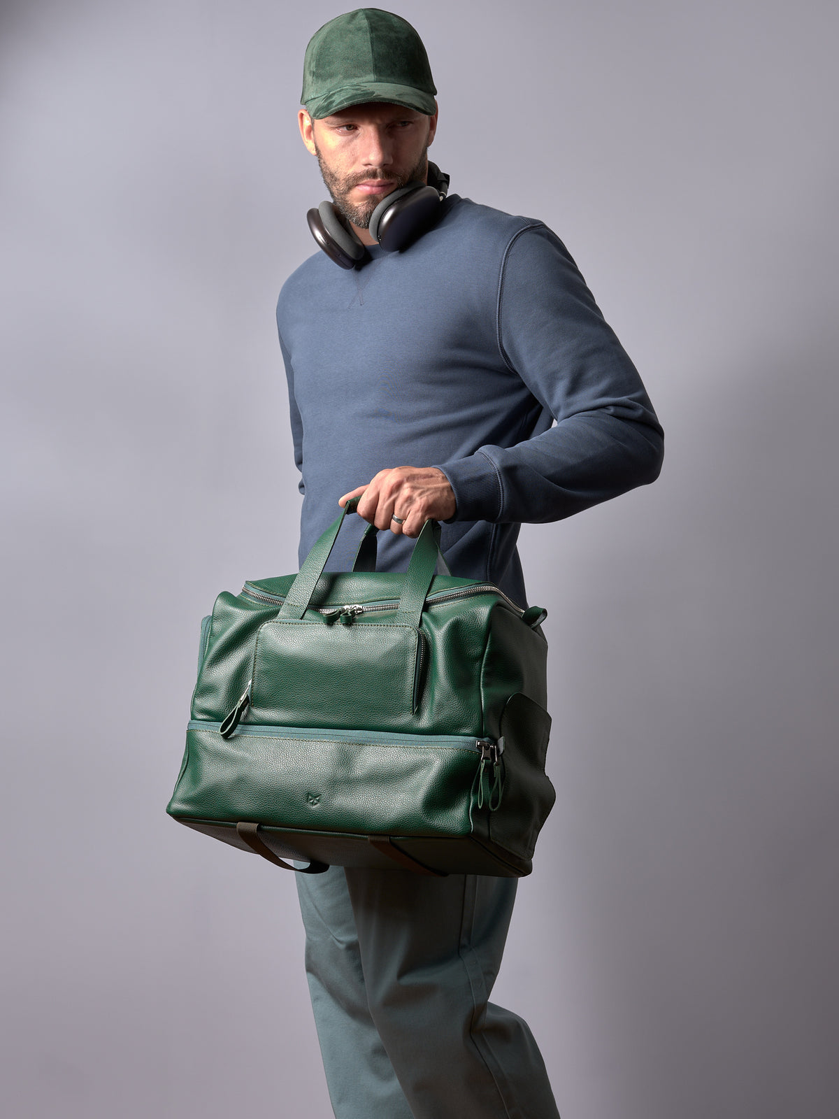 Man with a cap and headphones holding the Capra Leather Ventra Holdall, a green leather travel bag.