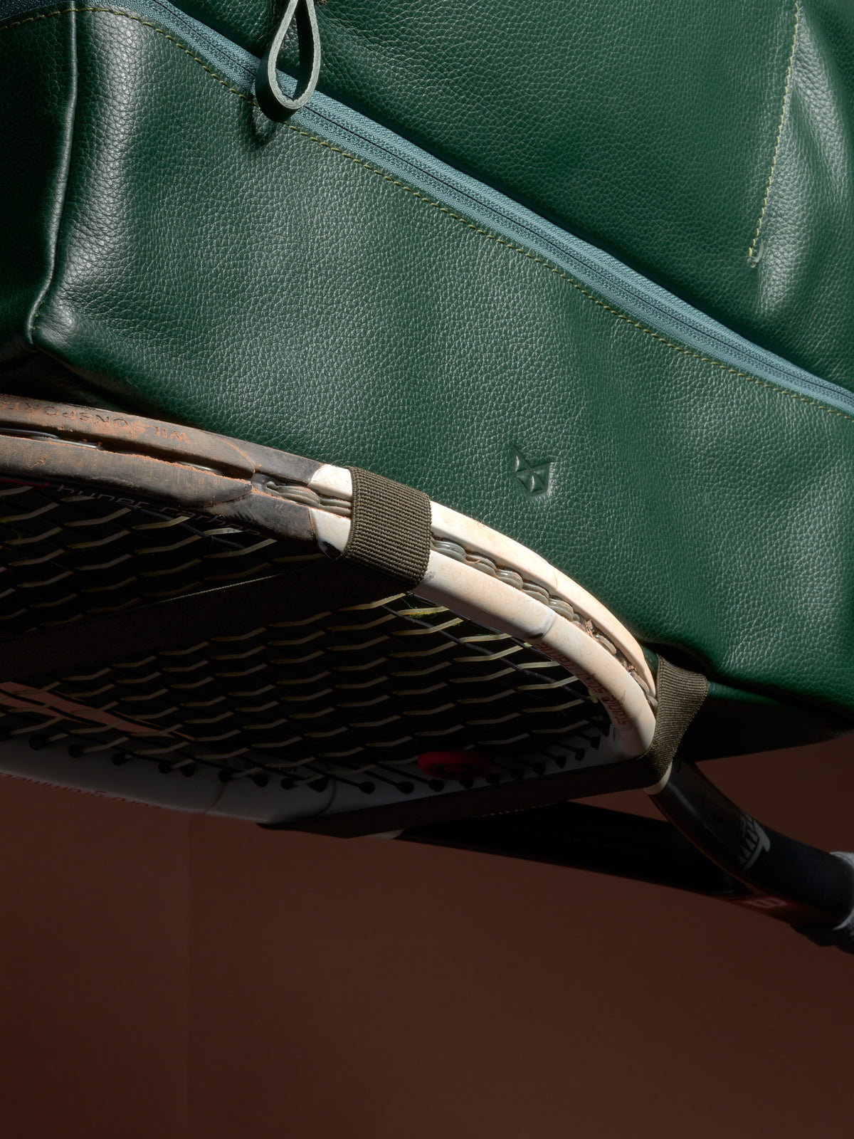 Close-up of the Ventra Holdall's versatile straps securely holding a tennis racquet against the green leather.