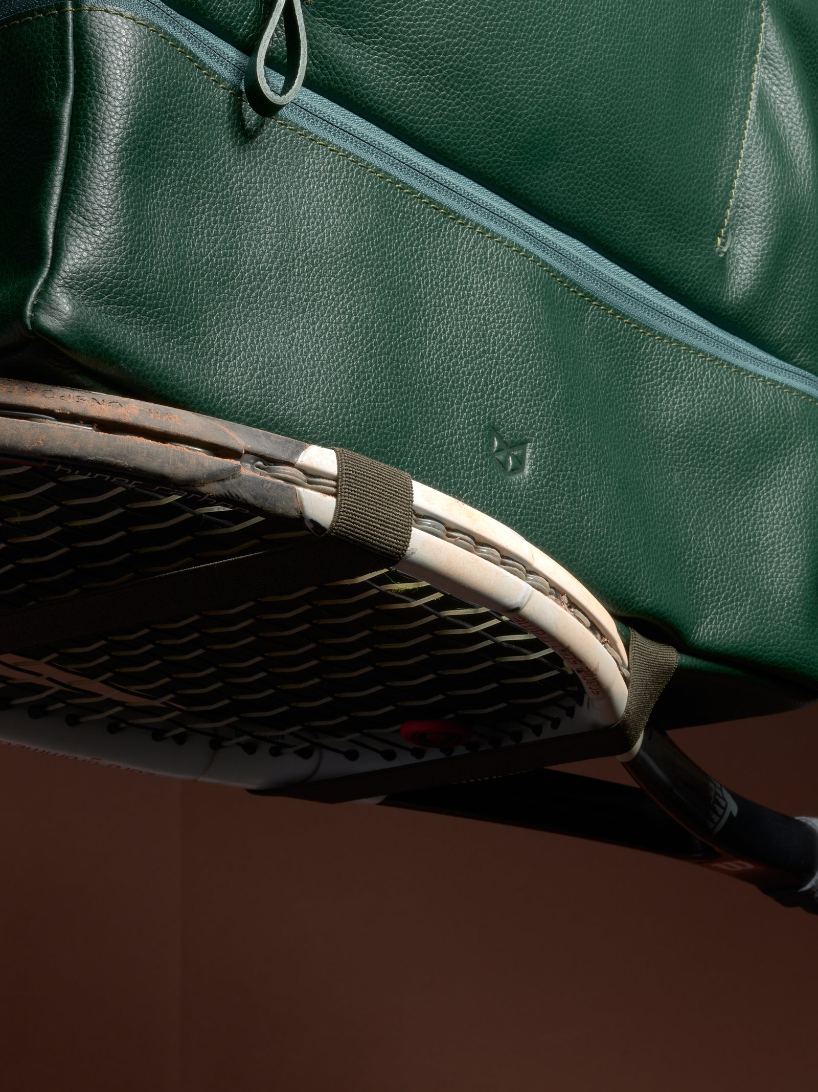 Close-up of the Ventra Holdall's versatile straps securely holding a tennis racquet against the green leather.