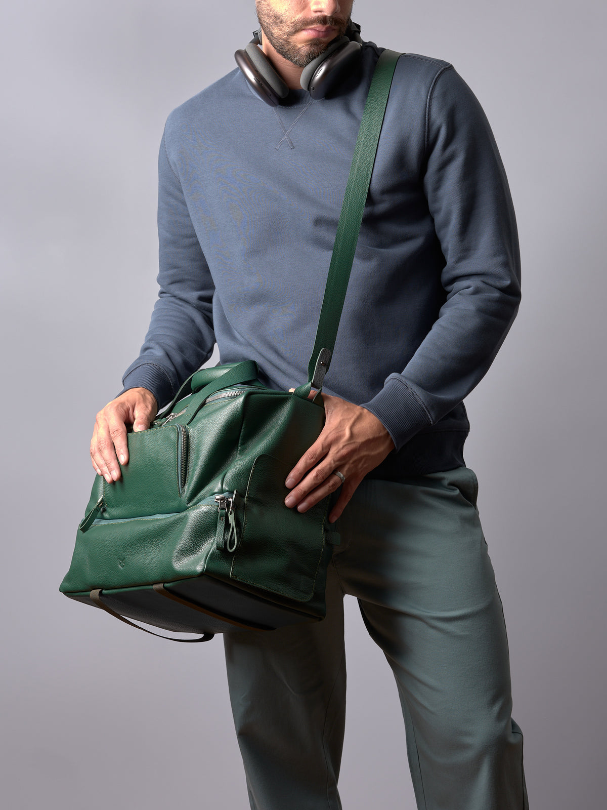 Close-up of a man's torso holding a green leather Ventra Holdall by Capra Leather with an adjustable shoulder strap.