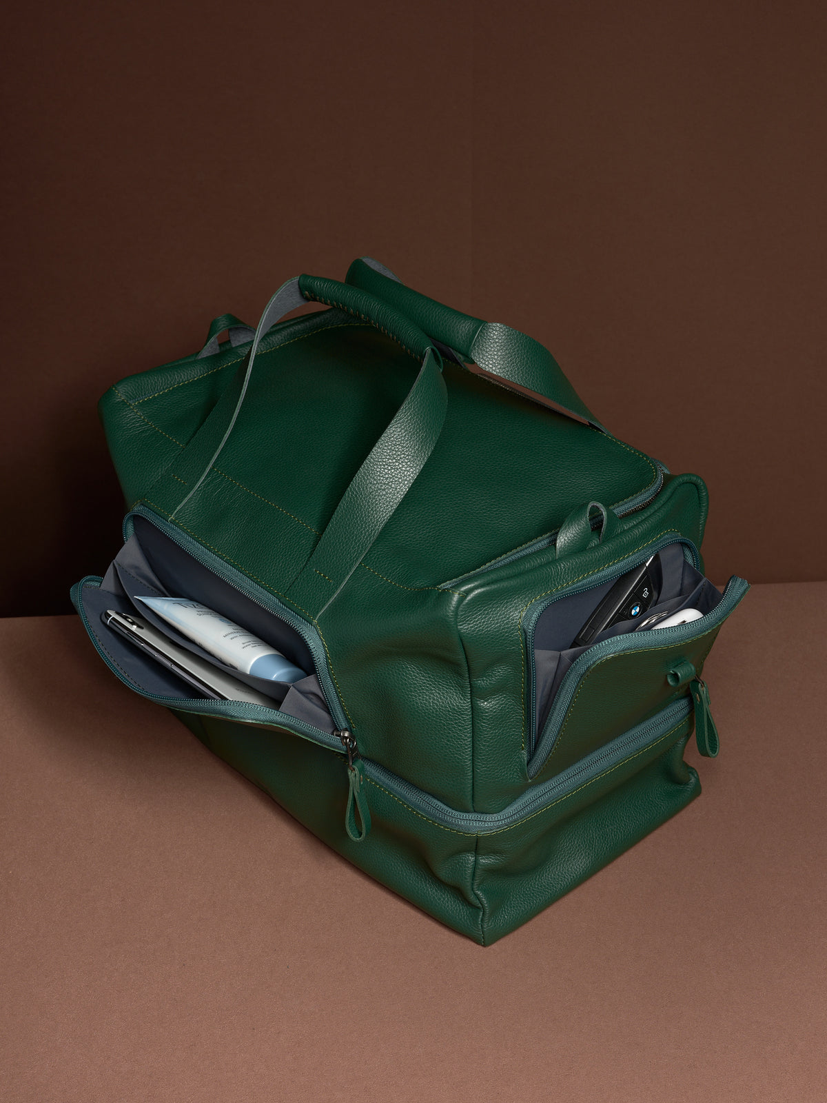 The green leather Ventra Holdall with its side wing pockets open, revealing organized storage for toiletries and gear.