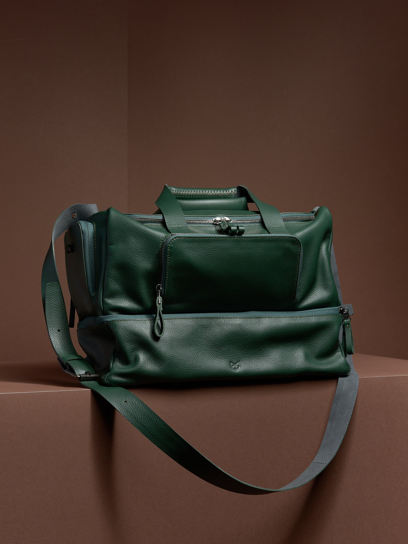 Man with a cap and headphones holding the Capra Leather Ventra Holdall, a green leather travel bag.