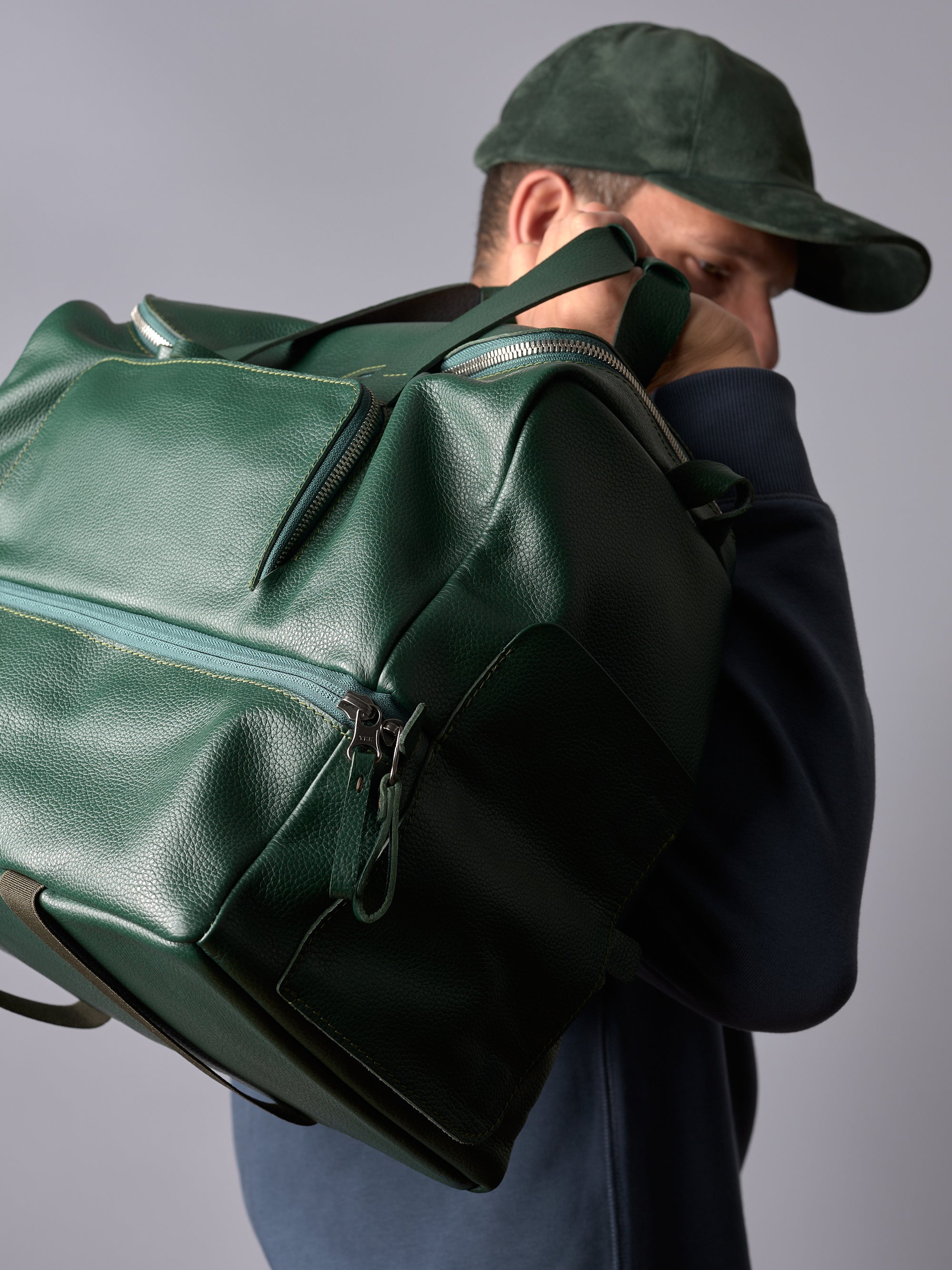 A man carrying a green leather Capra Ventra Holdall duffel bag on his shoulder, showcasing its spacious design.