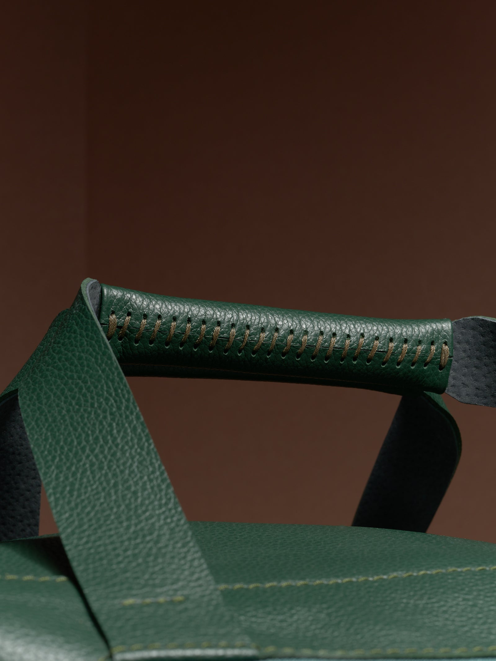 A detailed close-up of the hand-stitched handle on the green leather Ventra Holdall, showing quality craftsmanship.