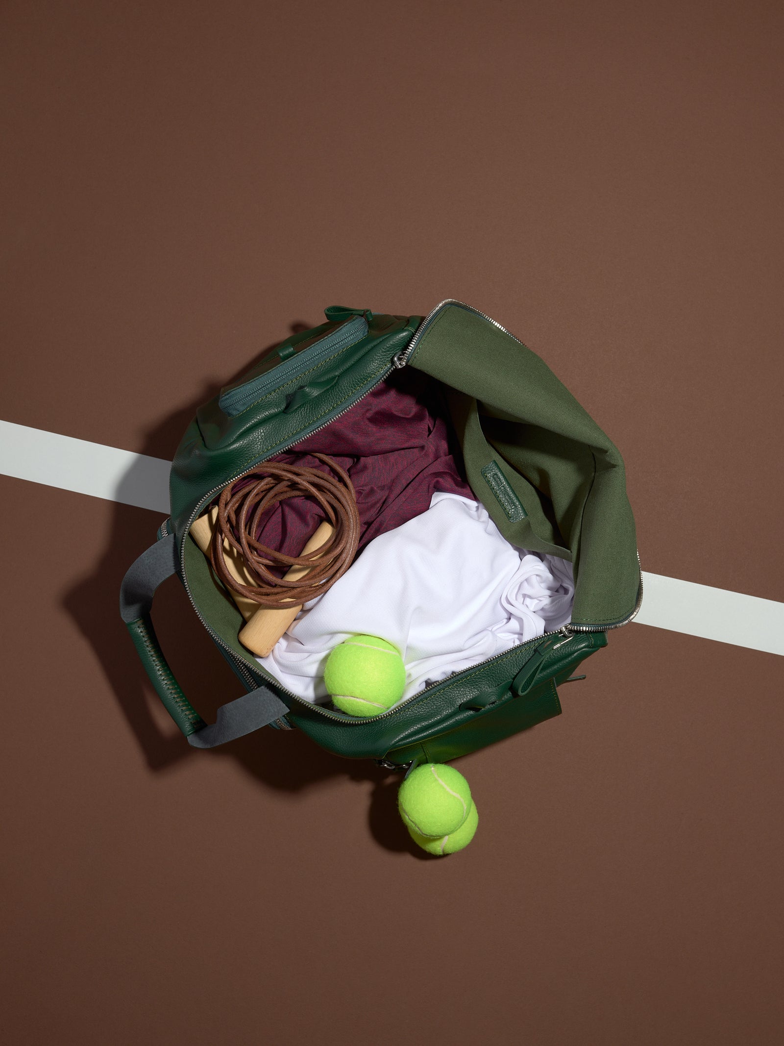 The open green leather Ventra Holdall used as a tennis bag, packed with clothes, a jump rope, and tennis balls.