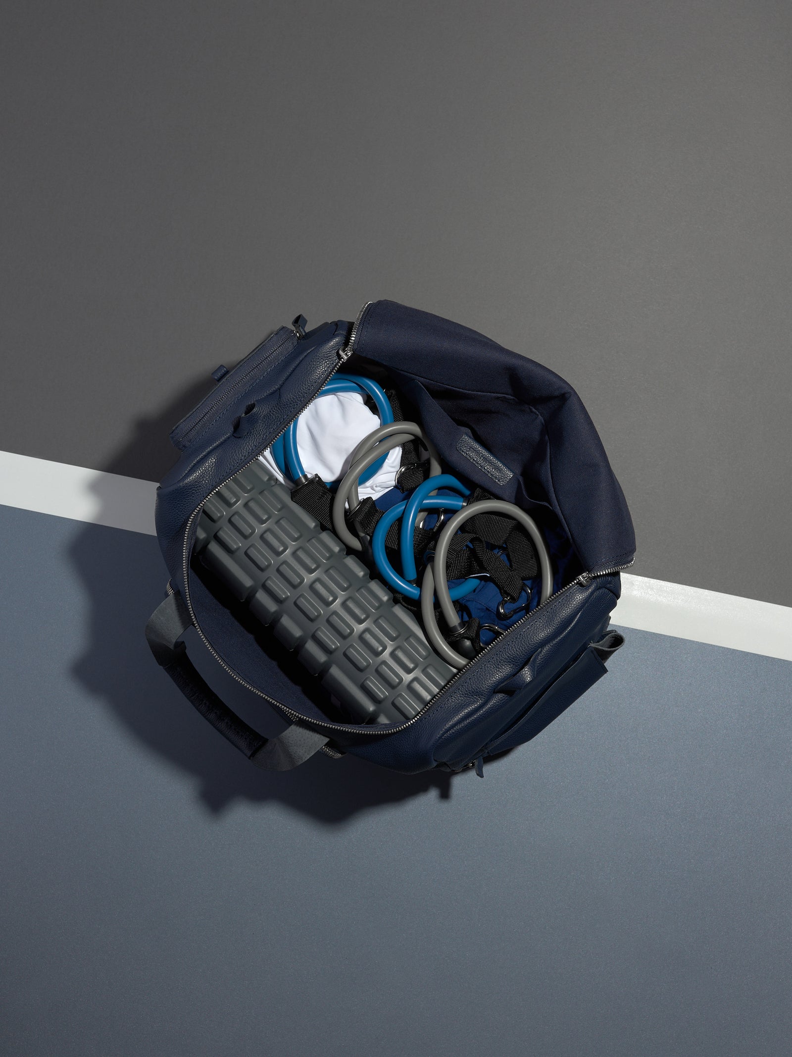 Navy leather Ventra Holdall bag on a grey platform with a strap draped down.