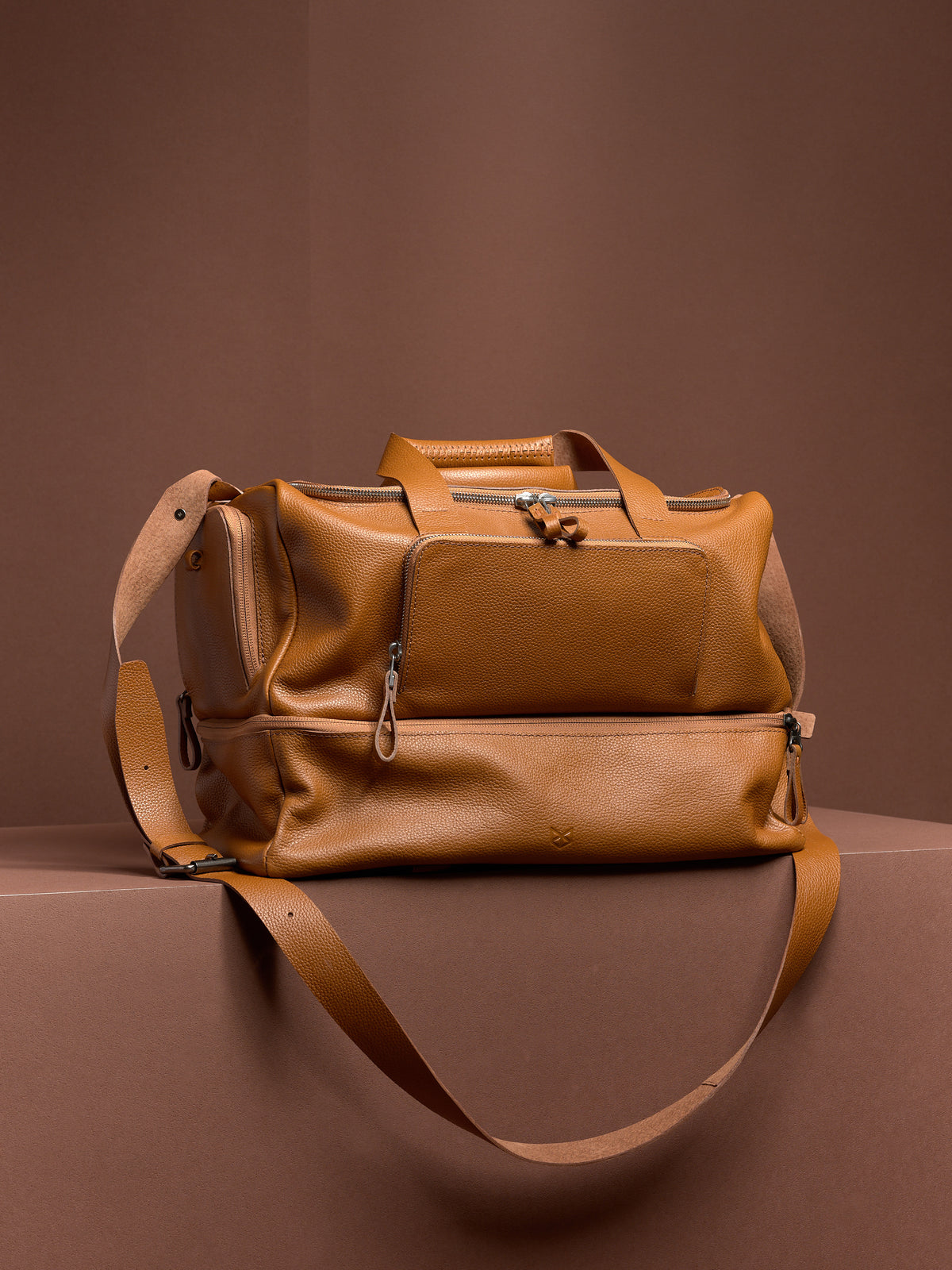 The tan leather Ventra Holdall weekender bag for men, shown with its shoulder strap, highlighting its classic duffel shape.
