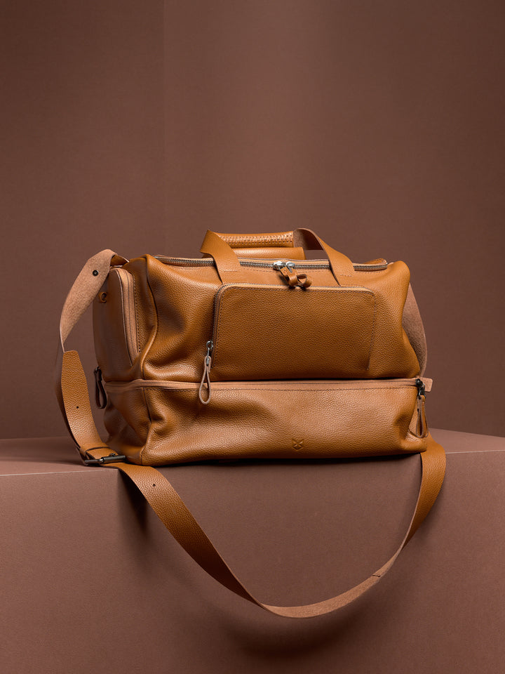 The tan leather Ventra Holdall weekender bag for men, shown with its shoulder strap, highlighting its classic duffel shape.