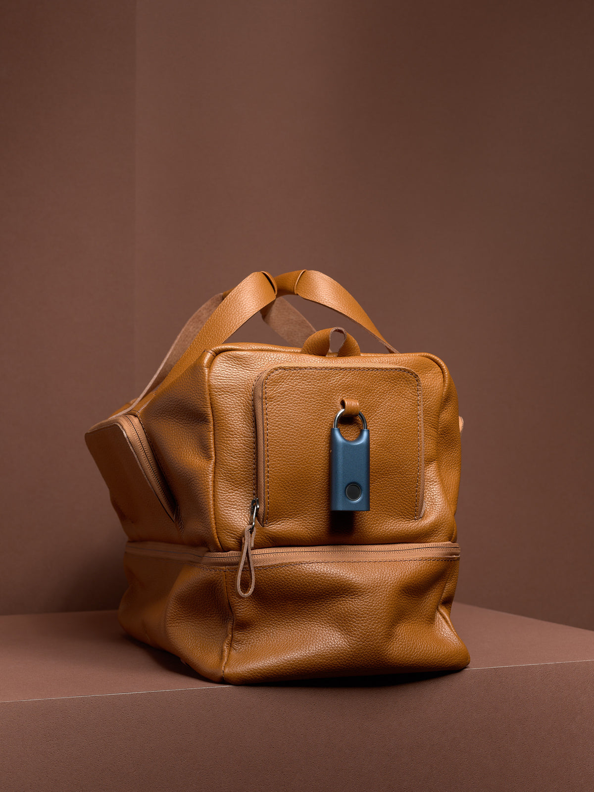 The tan leather Ventra Holdall with a blue tracker attached to the front pocket's purpose-built leather loop for security.
