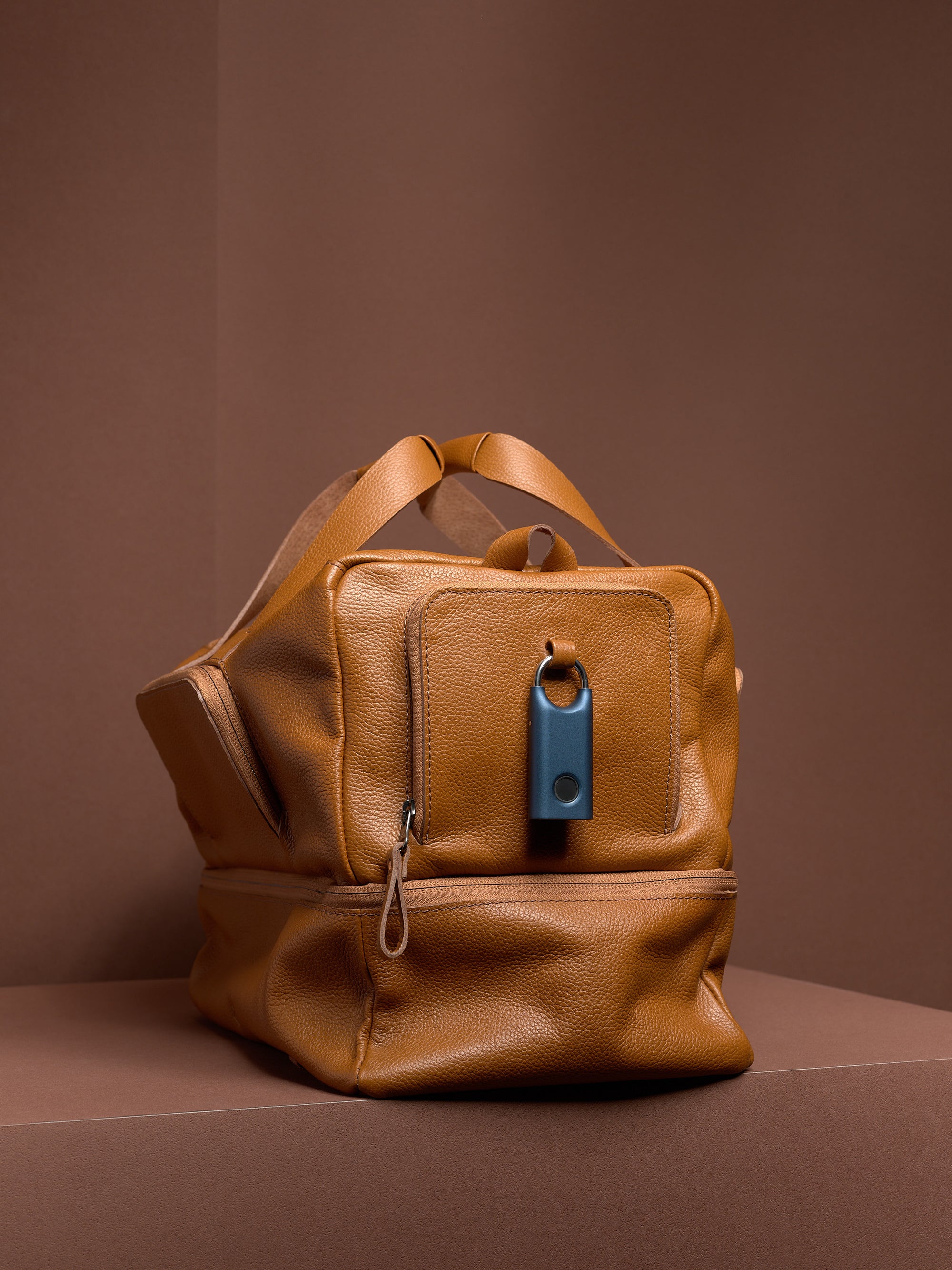 The tan leather Ventra Holdall with a blue tracker attached to the front pocket's purpose-built leather loop for security.