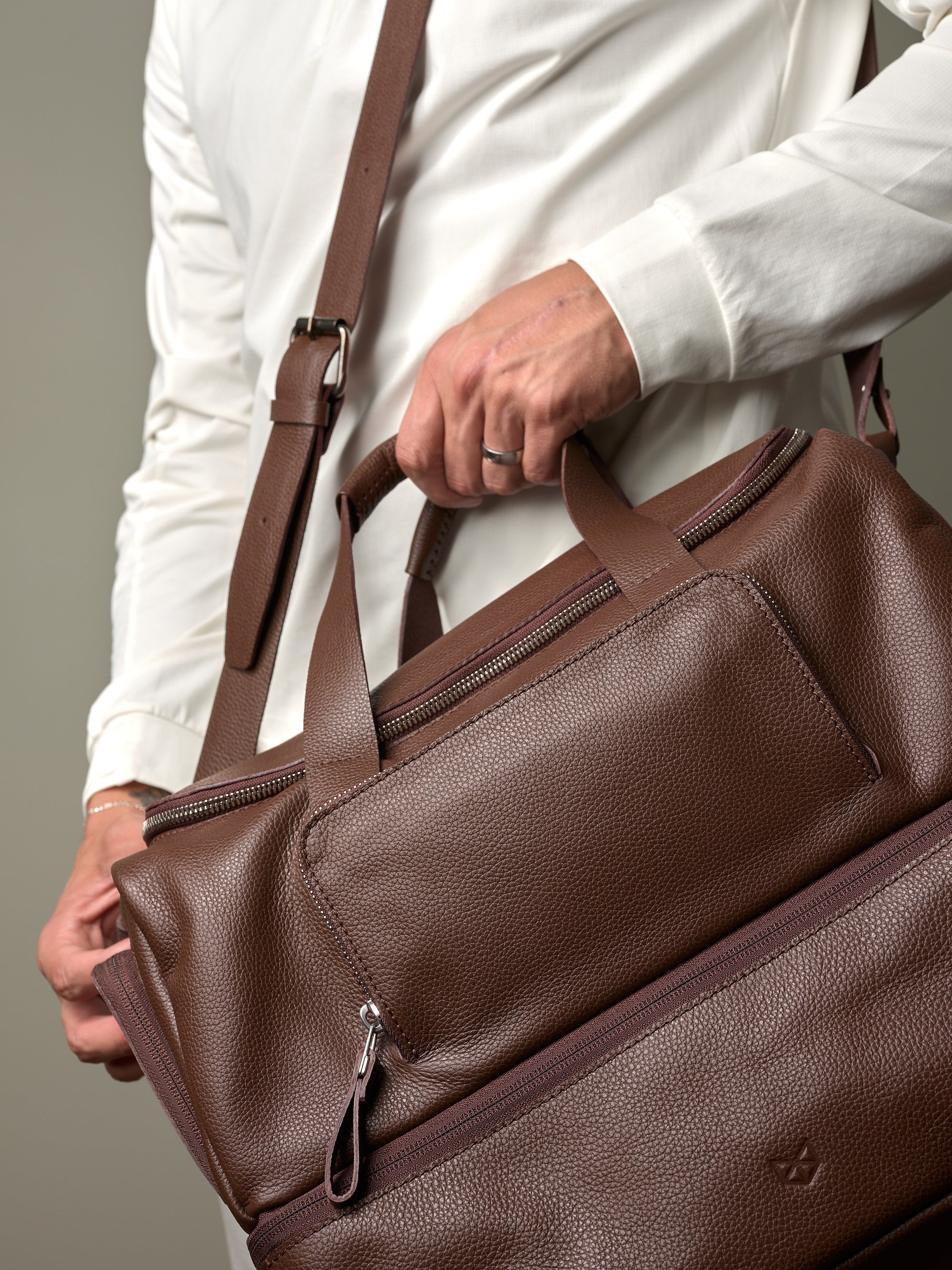 Close-up of a man's hands holding the brown leather Capra Ventra Holdall, highlighting the rich texture and zippered pockets.