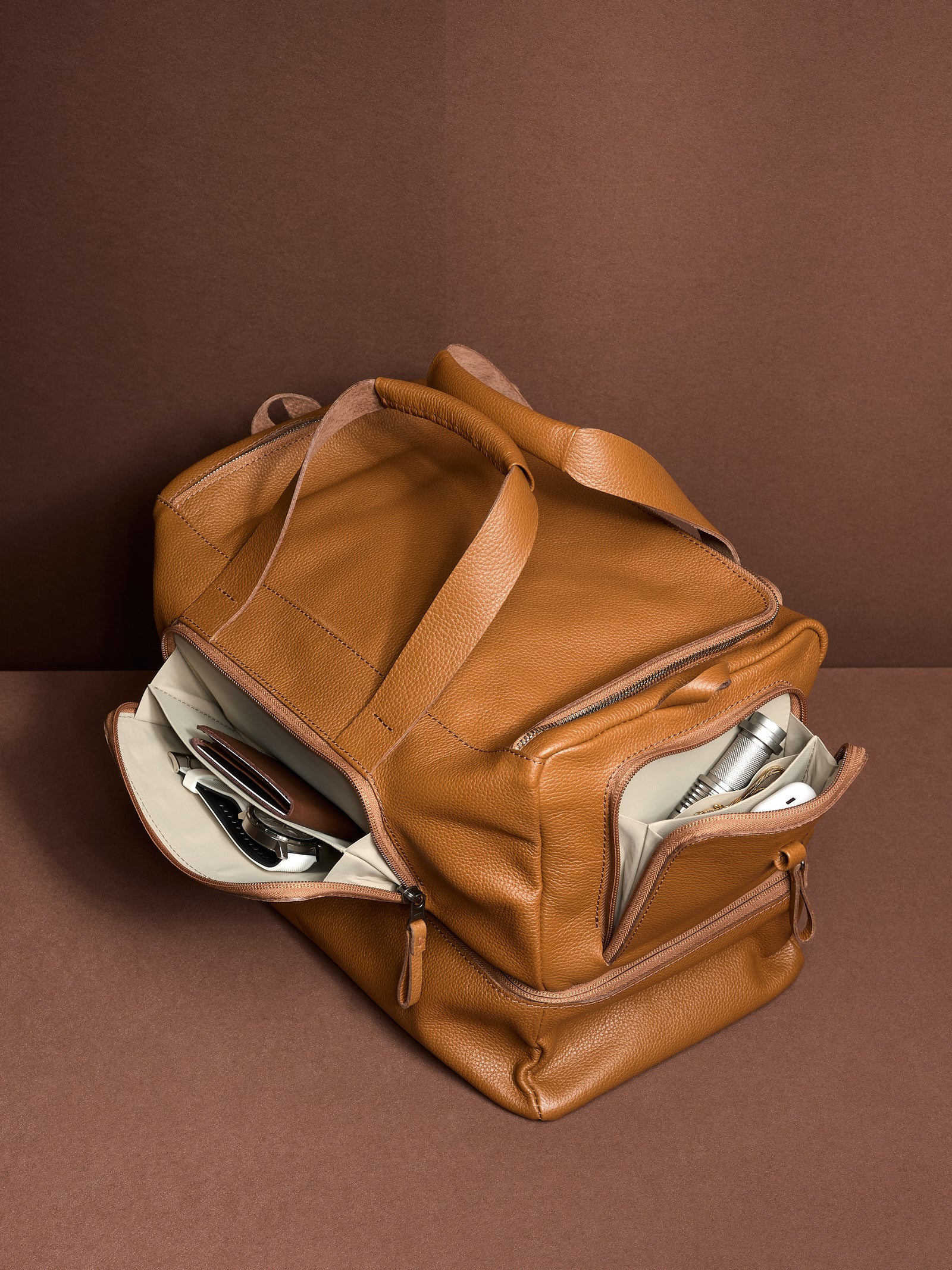 The tan leather Ventra Holdall's two large side pockets are open, showcasing the bag's organized storage capabilities.