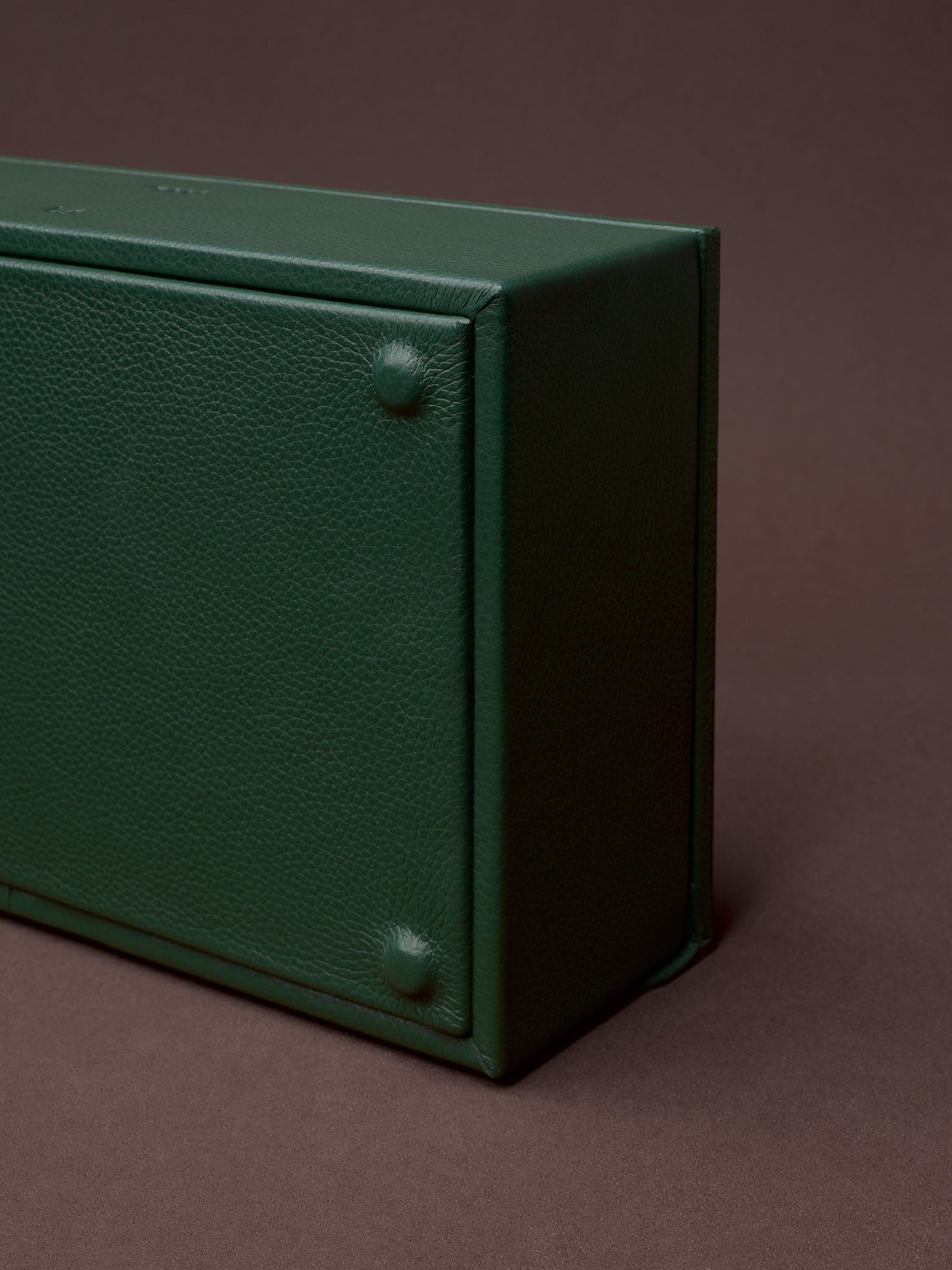 Close-up of the bottom and side of a luxurious green full-grain leather watch box.