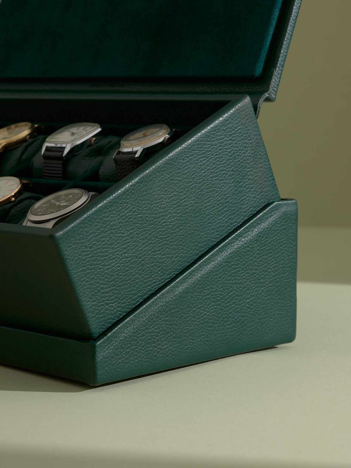 Close-up side view of the textured green leather watch box nesting flush into its angled display base.