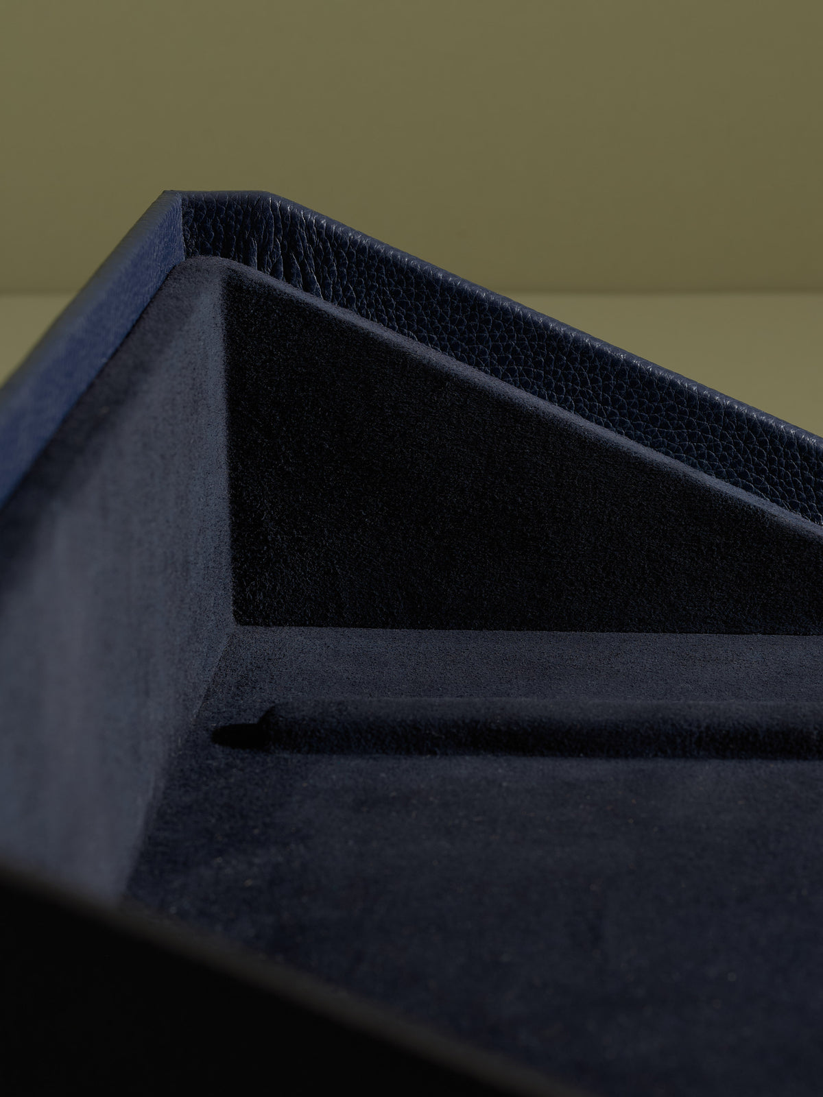 Close-up showing the precise stitching and plush navy blue suede lining of the angled leather valet drawer.