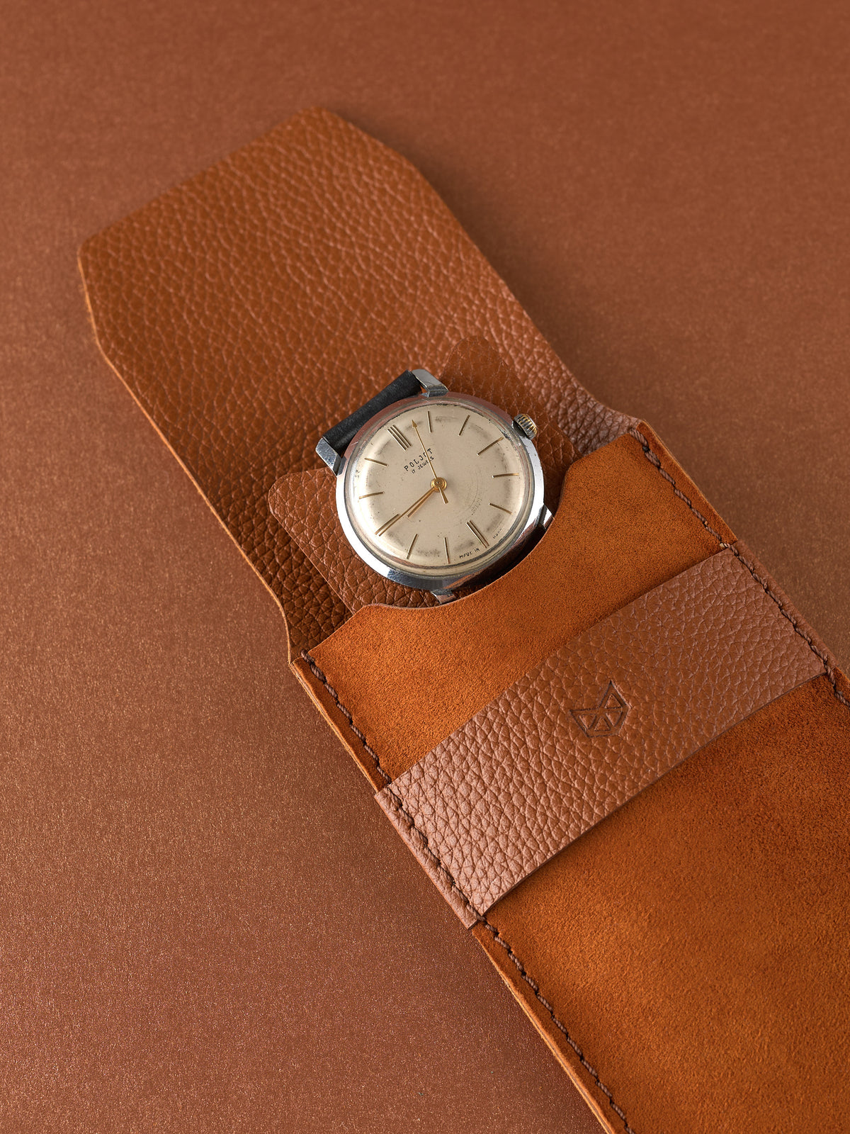 Men's vintage dress watch on a small tan leather insert with a Capra Leather watch pouch in the foreground.