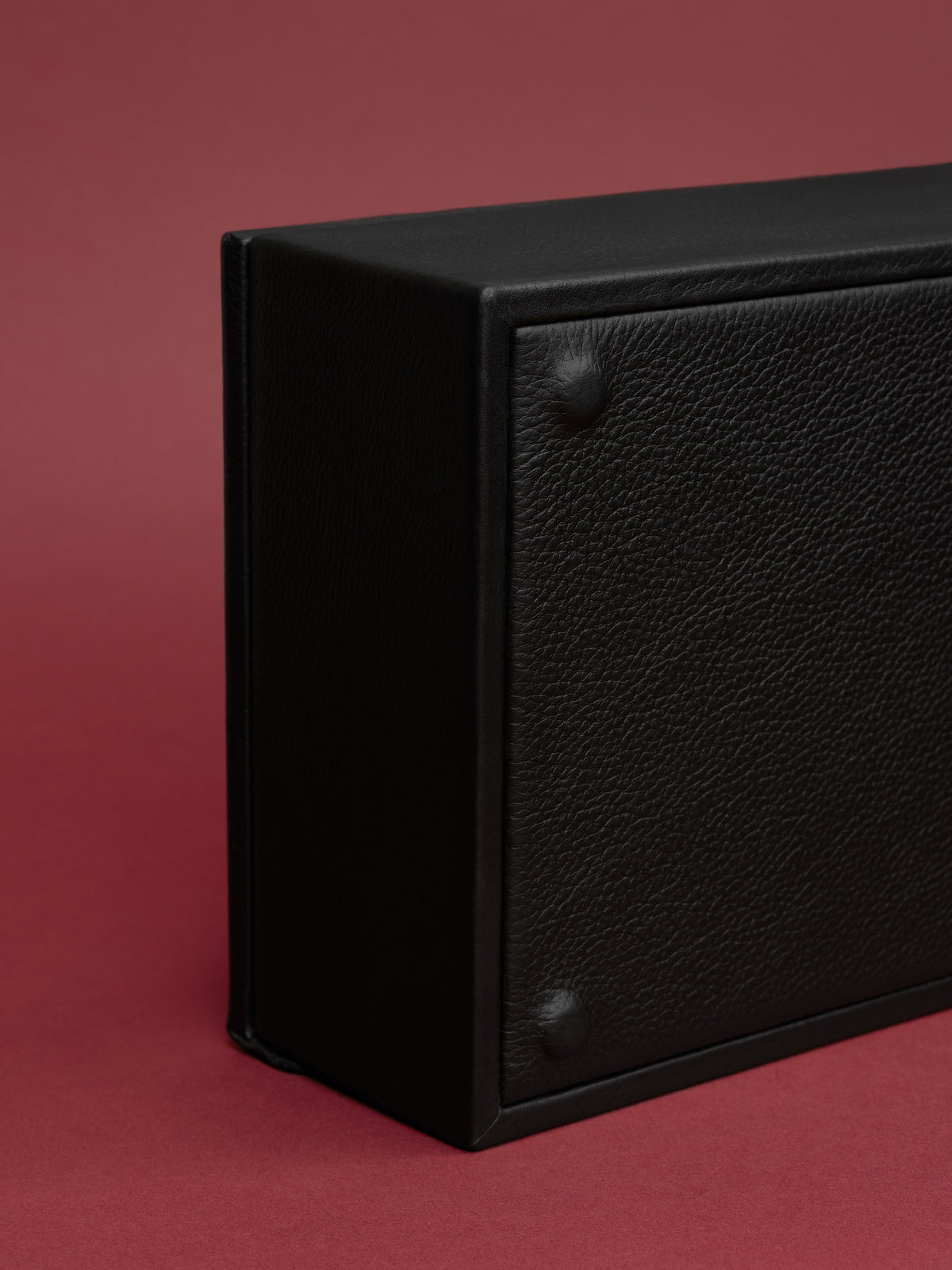 Detail of the structured black leather watch box showing the pebbled texture, corner rivets, and solid construction.
