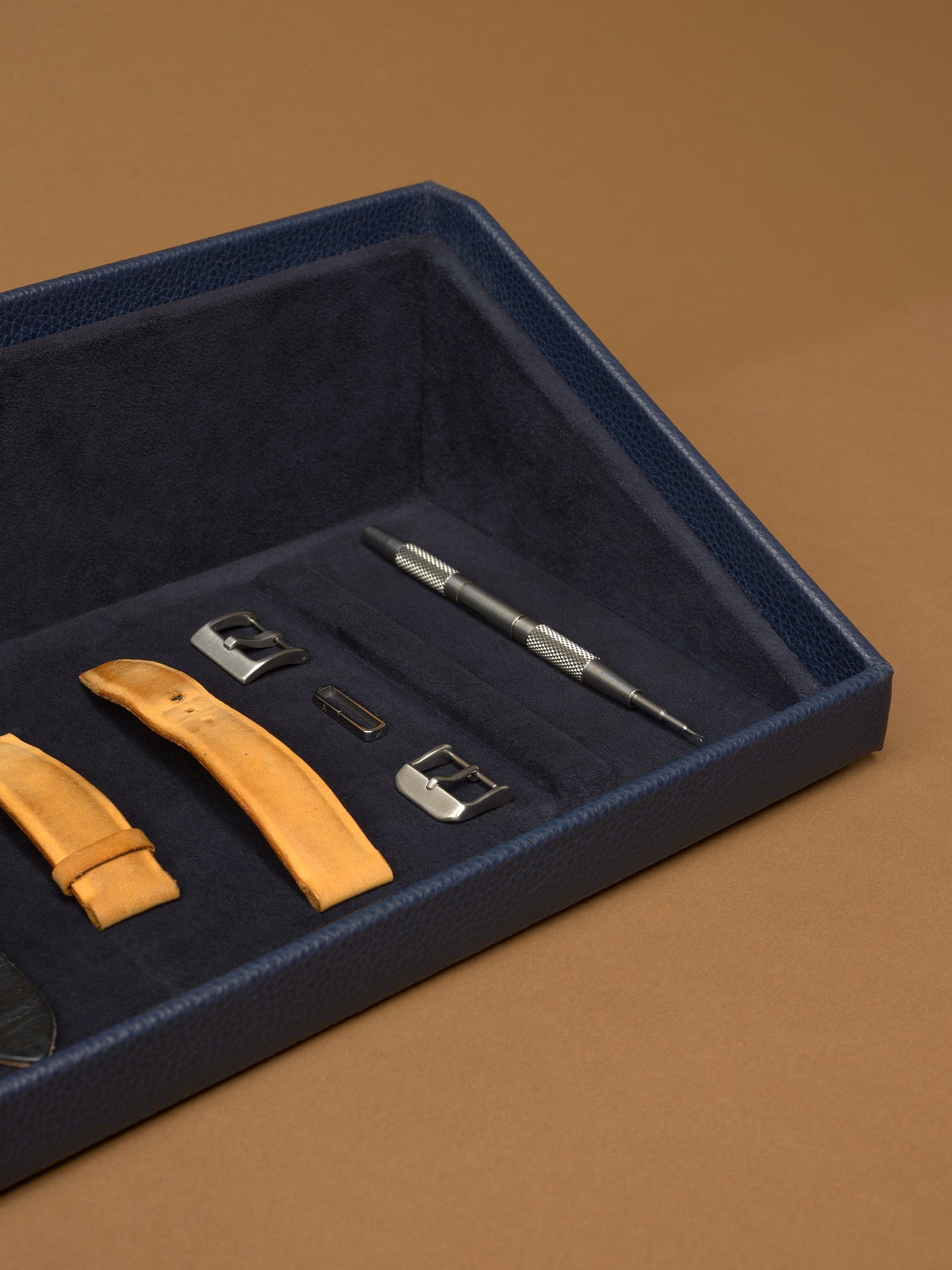 The Podium Open accessory storage drawer from the Capra leather watch box, showing watch straps and tools.