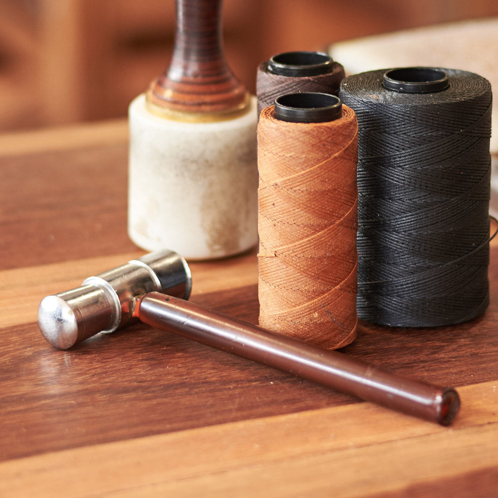 Spools of waxed thread, a hammer and an edge tool on a leatherworking bench