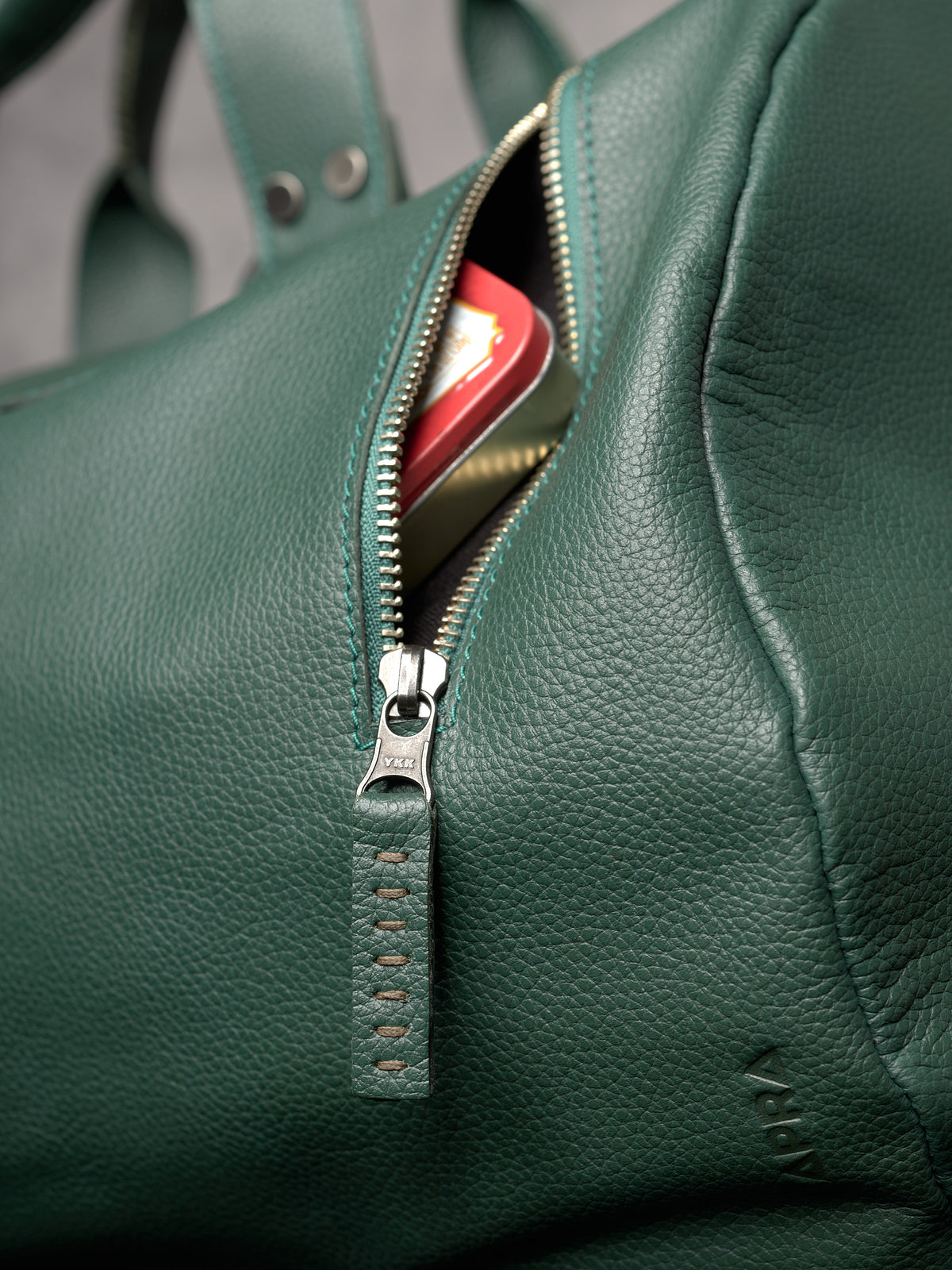 Close-up of a YKK zipper with a hand-stitched green leather pull and embossed brand logo.