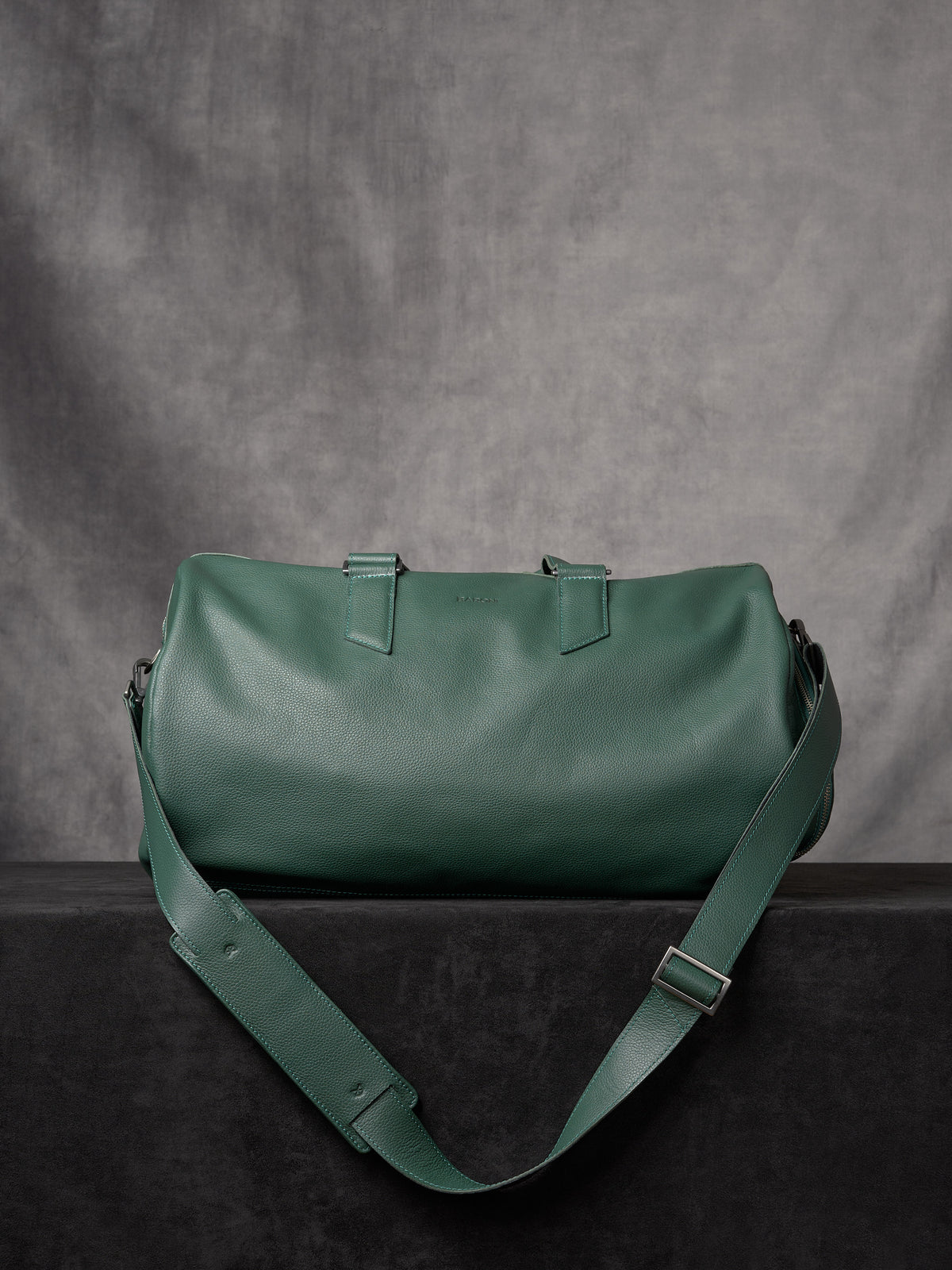 Full view of the forest green leather duffle bag showing the adjustable shoulder strap and pebbled texture.