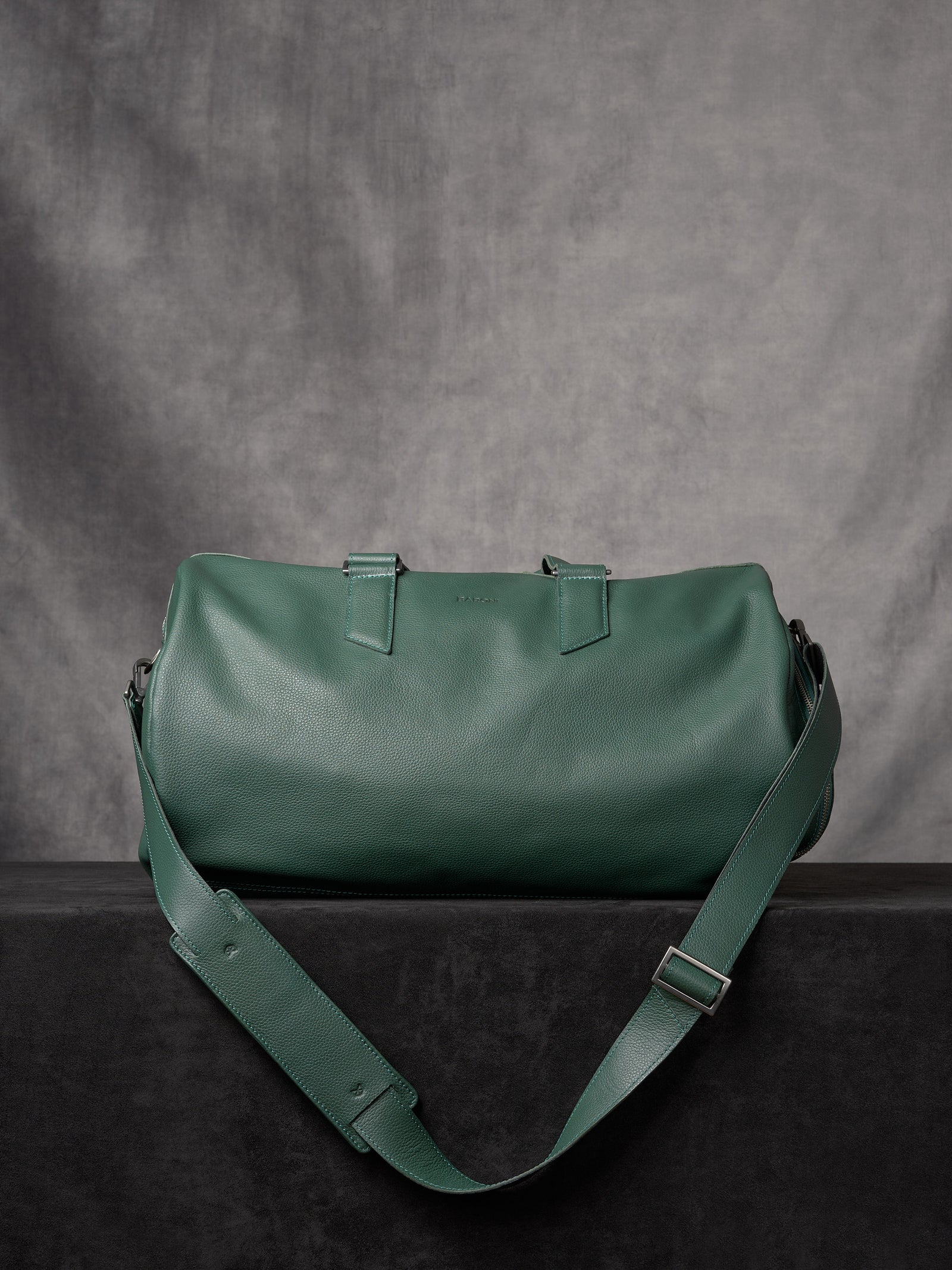 Full view of the forest green leather duffle bag showing the adjustable shoulder strap and pebbled texture.