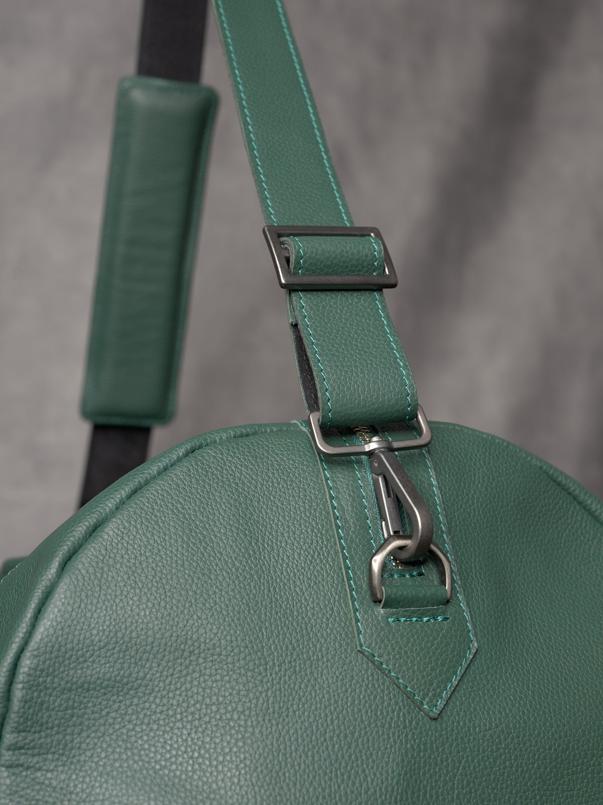 Detail shot of the heavy-duty metal carabiner and adjustable strap attachment on the green leather bag.